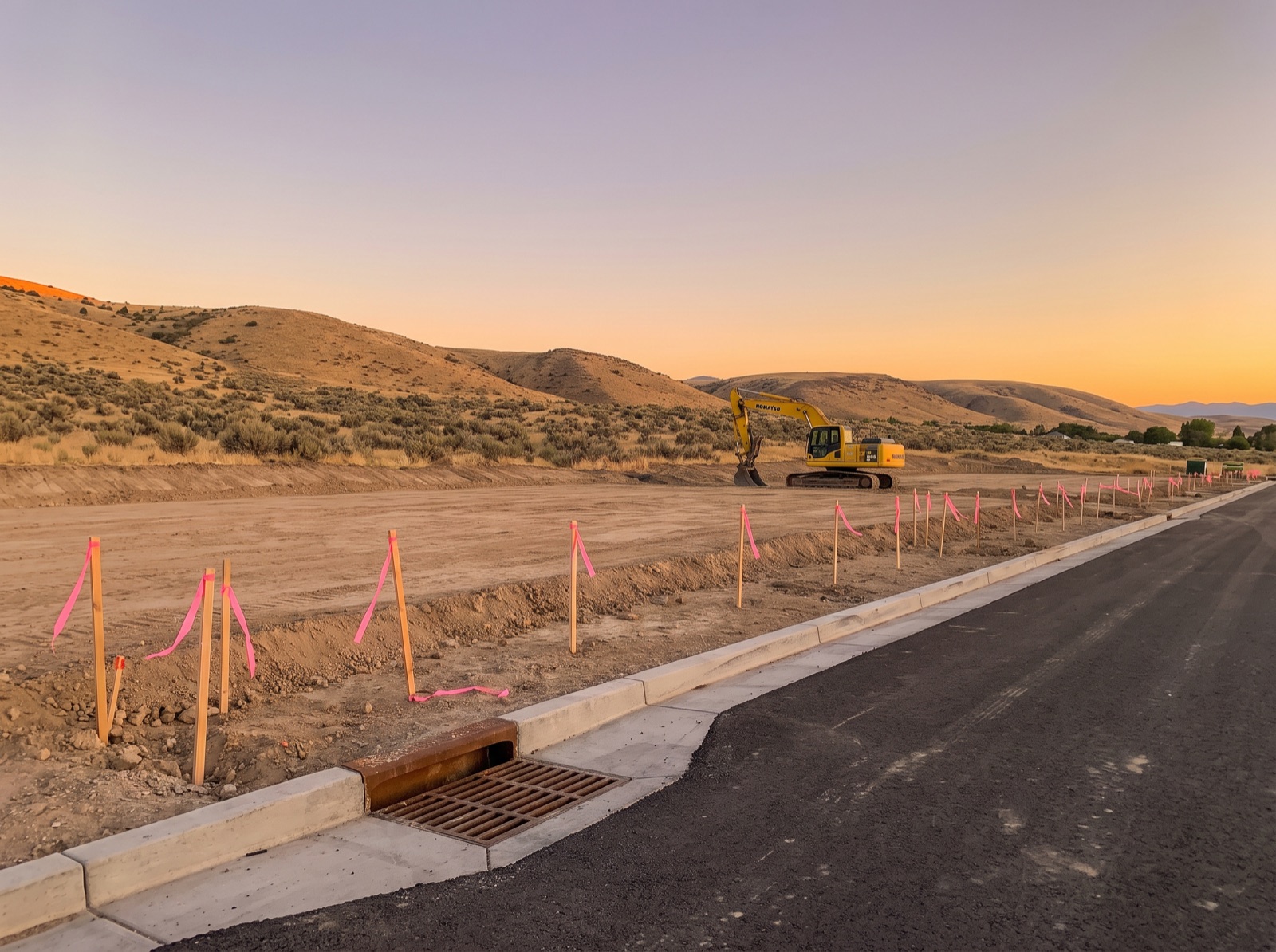 A newly graded pad and paved road with curb, gutter, and a storm drain inlet